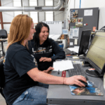 Jamie Noe working with another manufacturing team member at a computer.